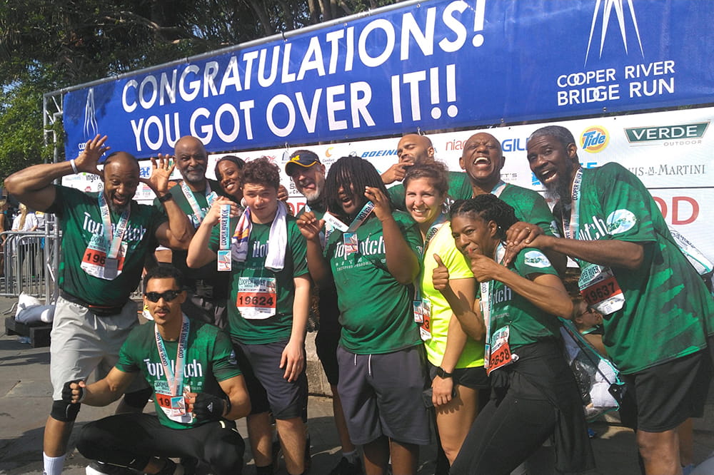 a group of runners makes silly faces and gives thumbs up in front of a sign that says Congratulations! You got over it! 