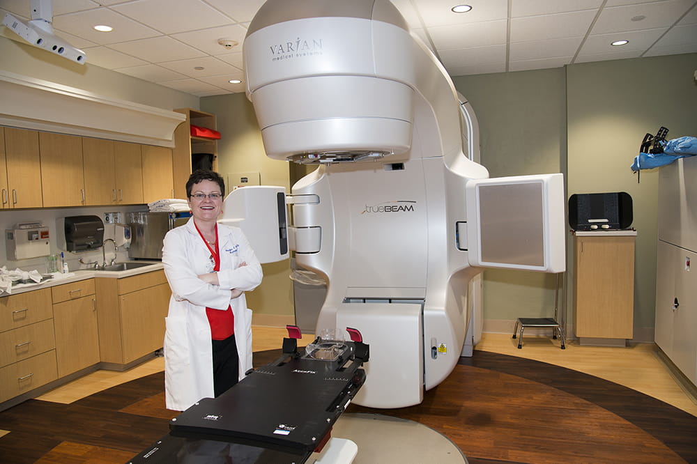 a woman poses in front of a radiation therapy machine