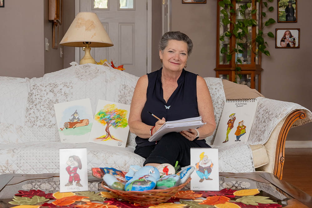 image of woman siting on sofa surrounded by her drawings and paintings