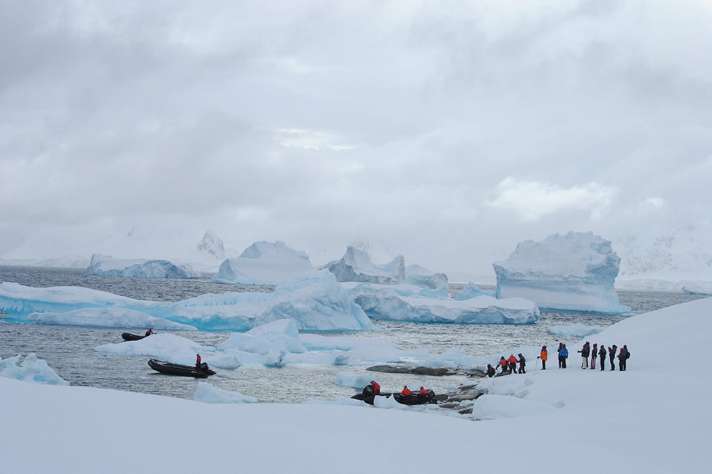 wide view of people lining up to get onto small boats surrounded by the vast ice and sky of Antarctica