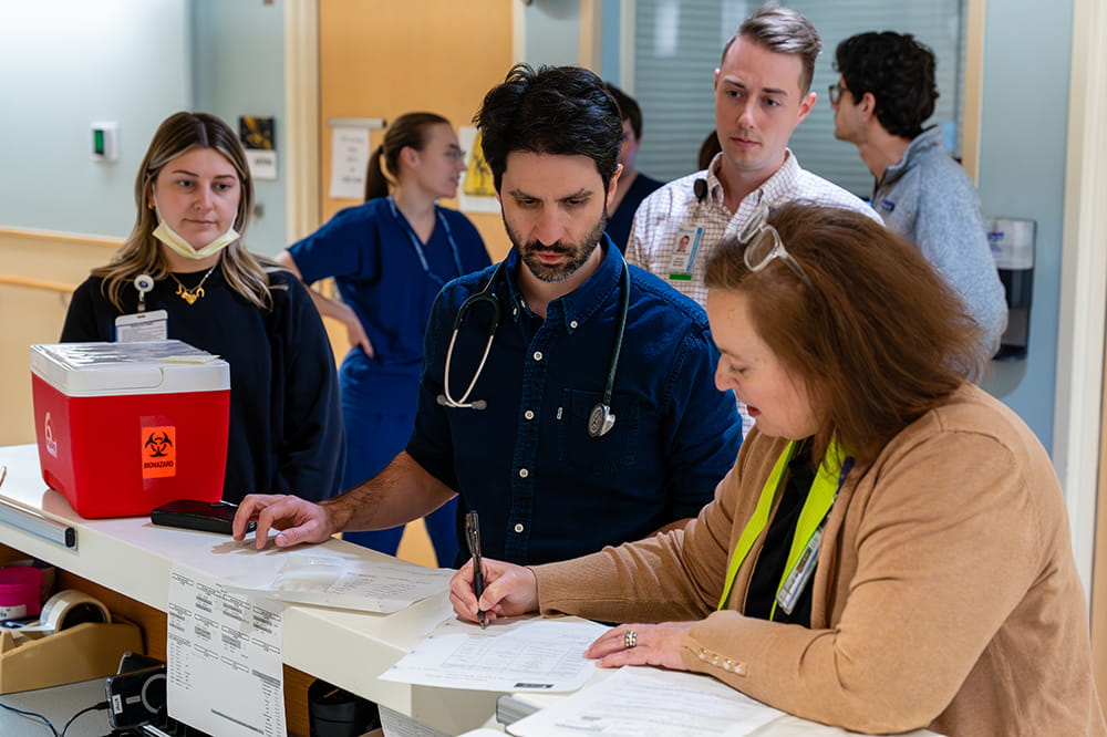 two people review paperwork at a nurses station while behind them the rest of the team waits