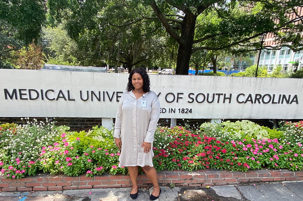 a woman poses in front of the Medical University of South Carolina sign on a summer-y day