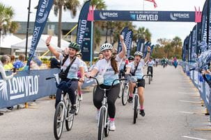 bicyclists raise their hands over their hands in triumph as they cross the LOWVELO finish line in 2023