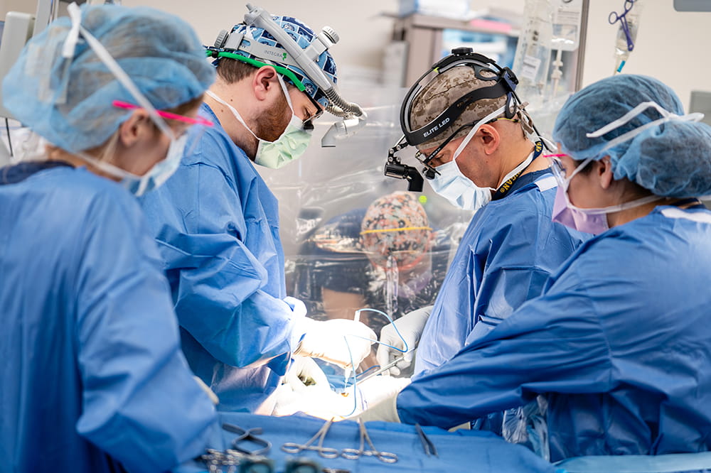 a doctor and nurse on each side of a patient in an operating room with an anesthesiologist just visible at the head of the table