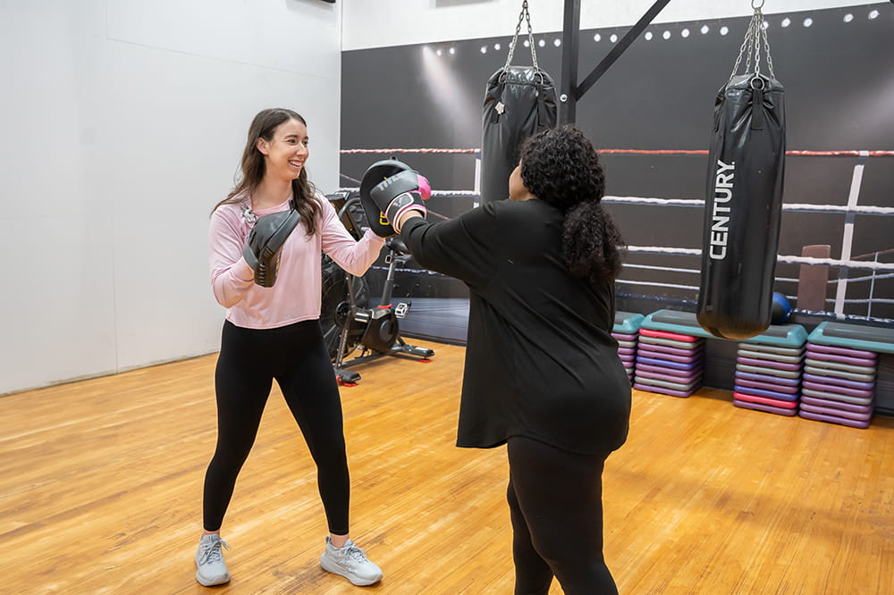 a young woman wearing boxing training pads works with a woman in a boxing studio