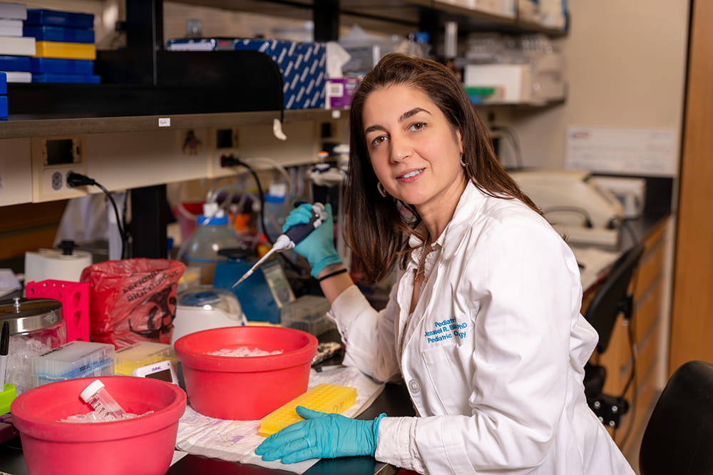 image of Jezabel Rodriguez Blanco in white lab coat and gloves sitting at the bench in her lab at Hollings Cancer Center