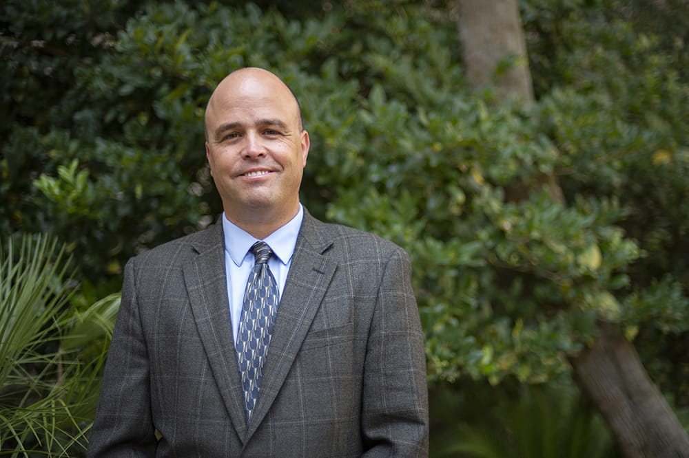 tobacco and vaping researcher Matthew Carpenter poses in a suit in lush green outdoor garden setting