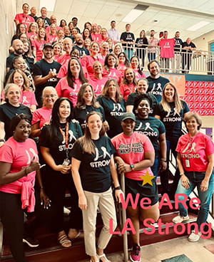 dozens of teachers in black or pink T shirts pose on stairs with We ARe LA Strong written atop the photo