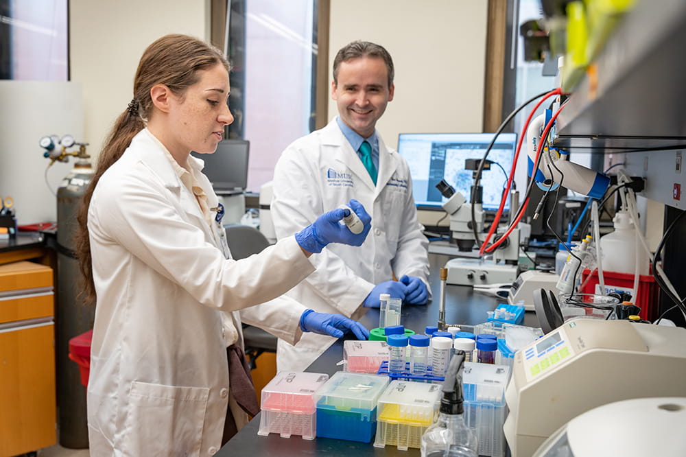 a man and woman in white lab coats in a lab setting talking and working