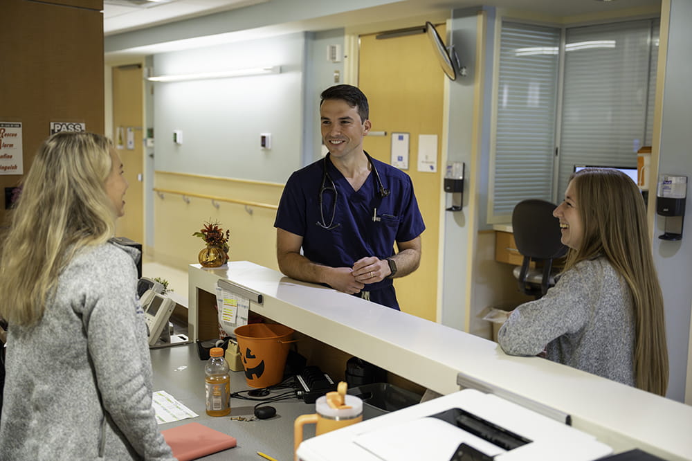 three young doctors stand around a nurses station to chat