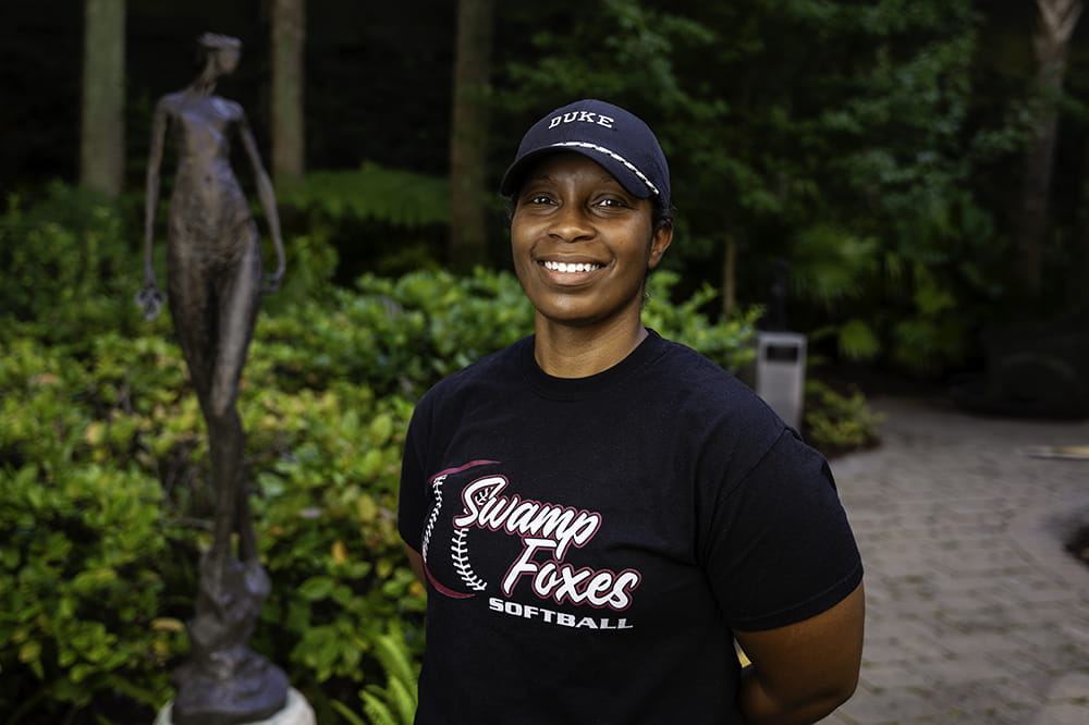 breast cancer patient Larissa Shannon poses in a ballcap and Swamp Foxes t-shirt in a garden setting