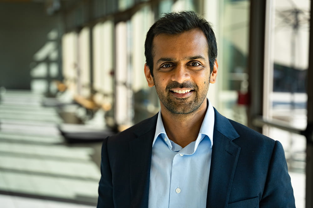 portrait of researcher Ashish Deshmukh in jacket and collared shirt open at the neck in a sunlit hallway