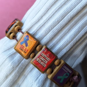 closeup of a bracelet made of wooden tiles with messages against cancer