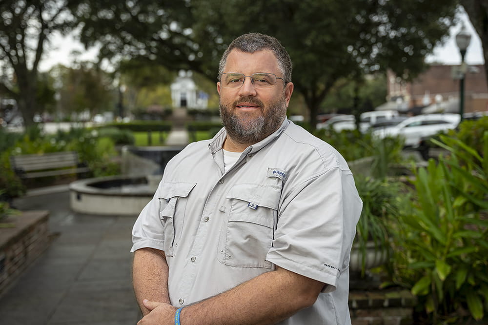 portrait of a man standing outside in a garden setting with a fountain in the background