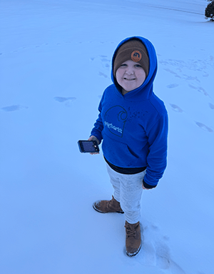 a young boy in Lowcountry cold weather gear grins up at the camera while standing in the snow