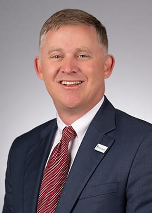 headshot of man in dark suit and red tie