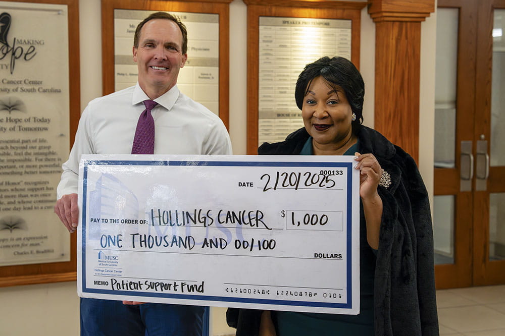 a man and woman smile from behind an oversized check written out to Hollings Cancer Center