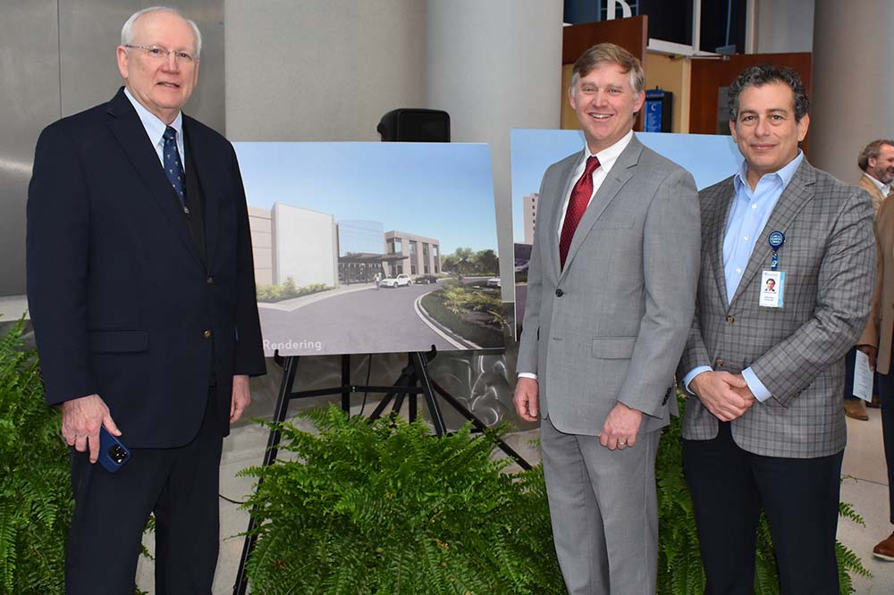 Three men in business attire stand beside a rendering of a building on a stand.