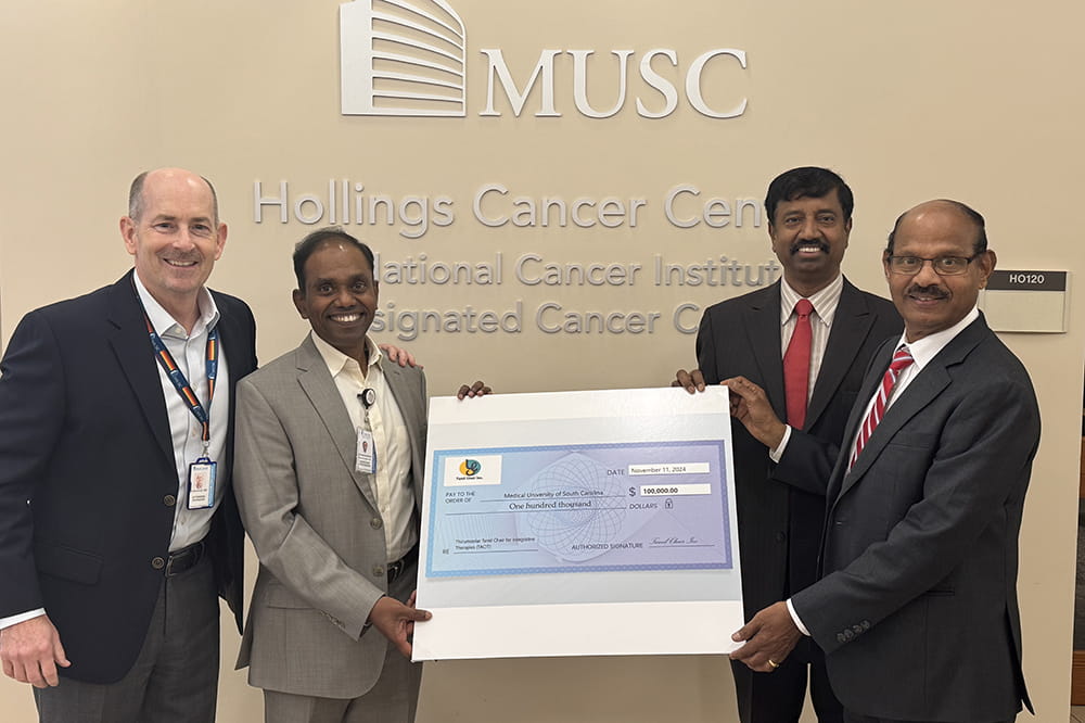 four men stand around an oversized check in front of the MUSC Hollings Cancer Center sign