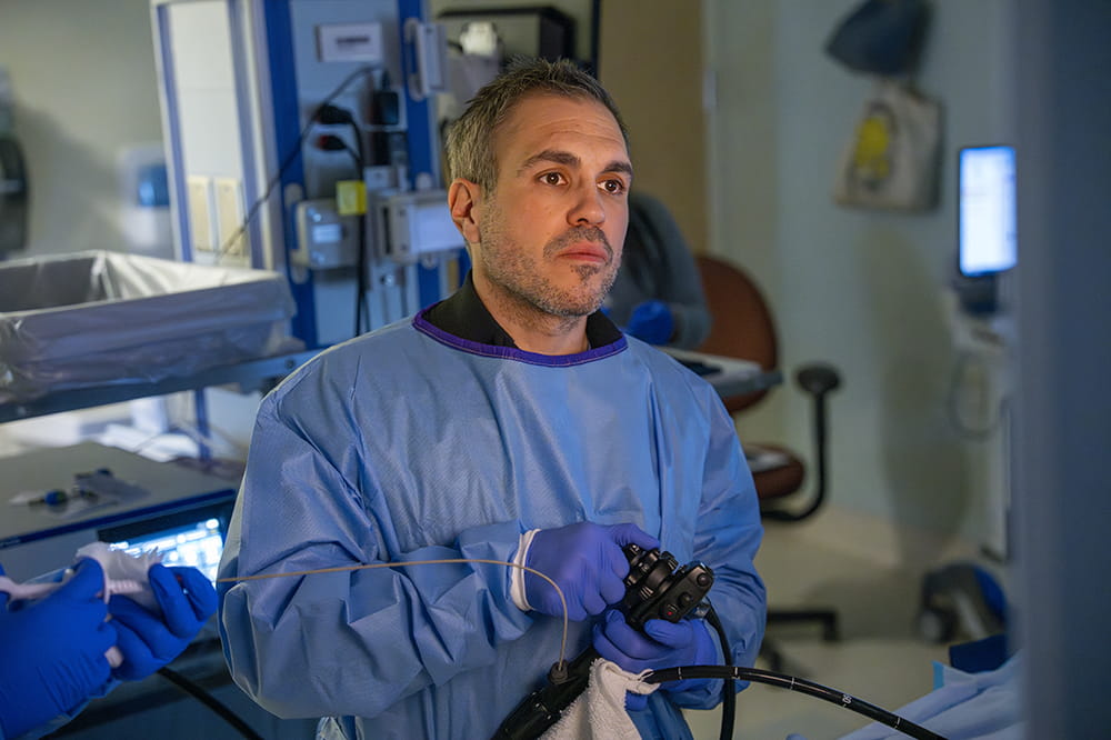 a gowned up doctor concentrates on a screen in front of him, off camera, during a procedure