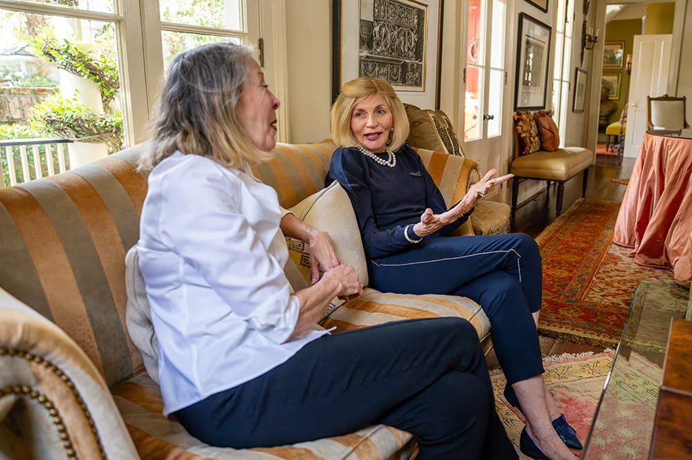 two elegant women sit on a sofa in a well appointed downtown Charleston home and chat