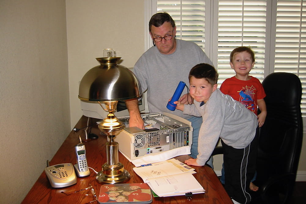 a man tinkers with some sort of electronic with two young boys helping