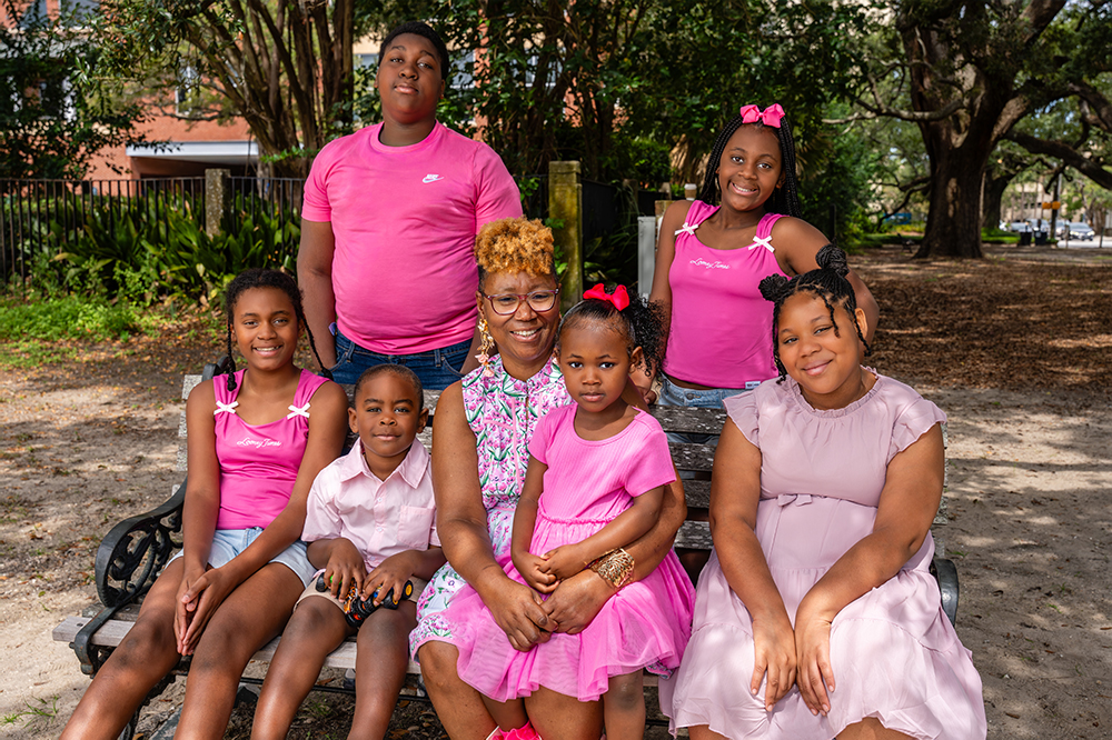 a woman sits surrounded by six children of various ages all wearing pink